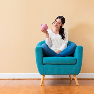 Woman sitting on a sofa and smiling at her piggy bank